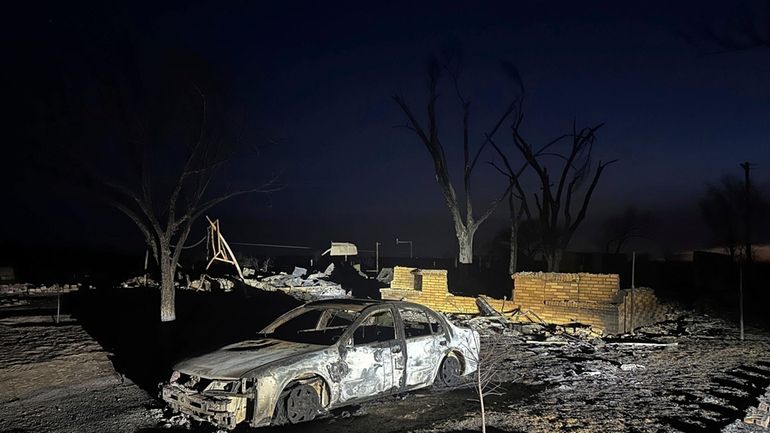 A charred vehicle sits near the ruins of a home...