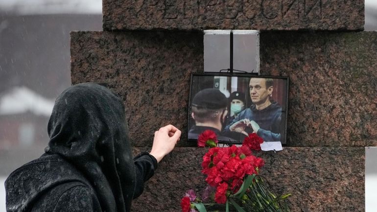 A woman touches a photo of Alexei Navalny after laying...