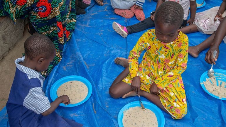 Children eat porridge prepared at a feeding center in Mudzi,...