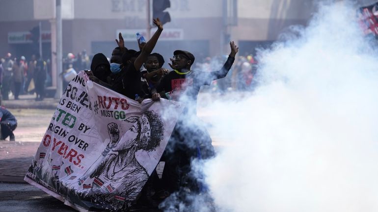 Protesters hide behind a banner as police fire teargas at...
