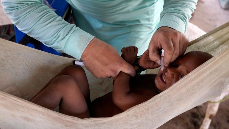 A health worker administers a polio vaccine to a child...