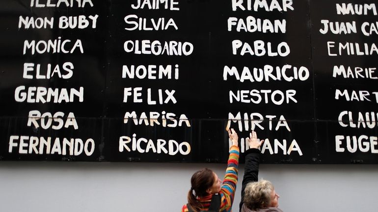 Women touch a board with the names of people who...