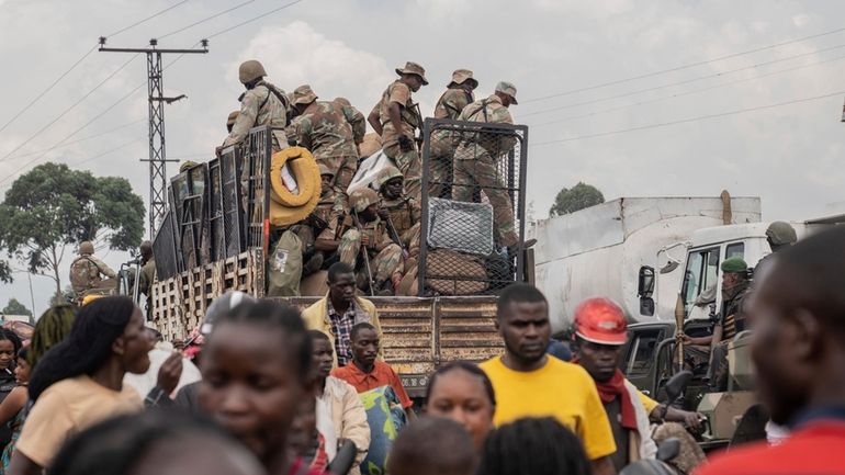 South African troops drive past thousands who are fleeing the...