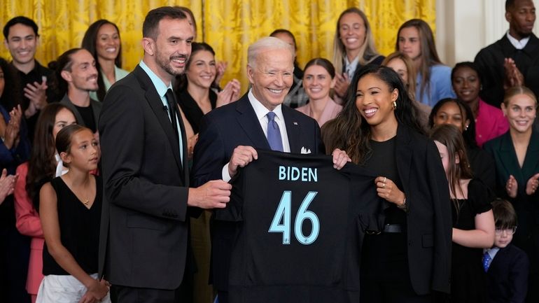 President Joe Biden, center, is presented with a team jersey...