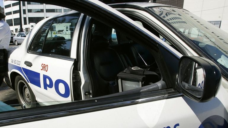 A New Orleans police officer leans against a patrol car,...