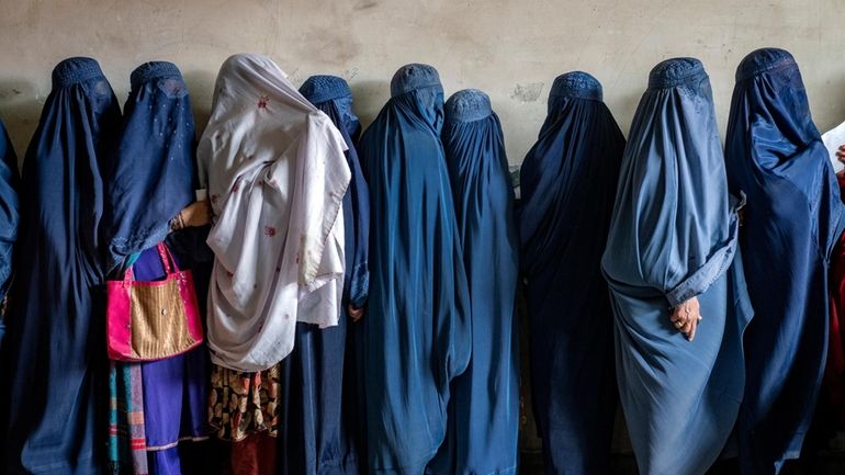 Afghan women wait to receive food rations distributed by a...