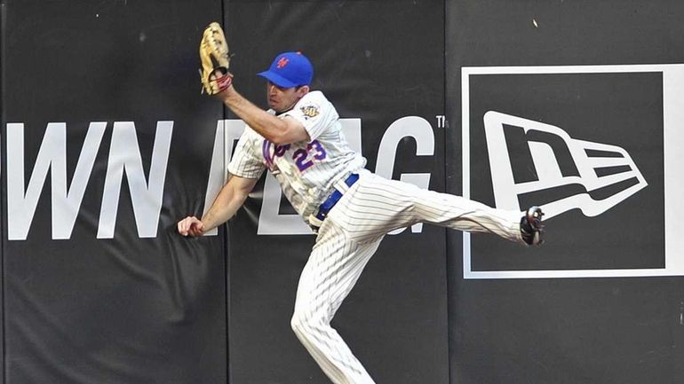 Mets left fielder Mike Baxter crashes into the wall after...