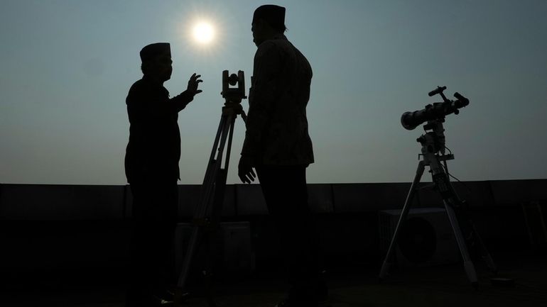 Officials are silhouetted as they use a telescope to scan...