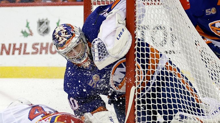Devils left wing Miles Wood crashes into Islanders goaltender Semyon Varlamov...