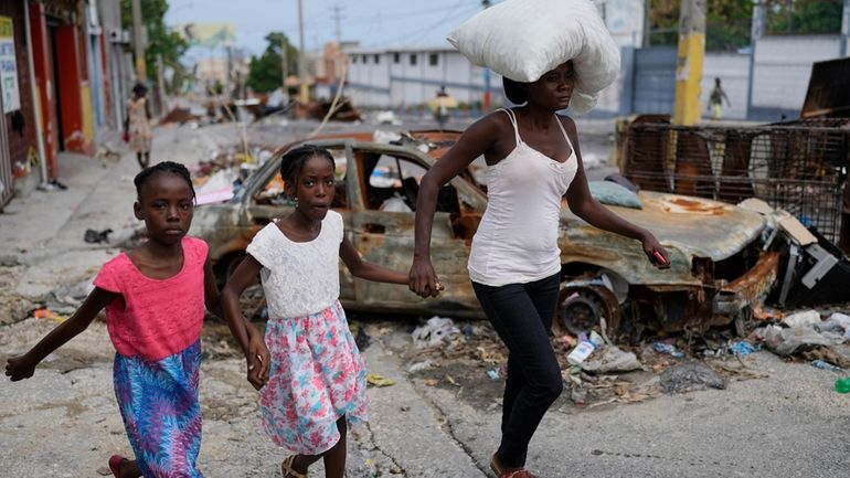 Residents walk past a burnt car blocking the street as...