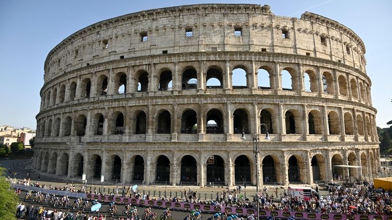 The pack of cyclists pedals past the ancient Colosseum, during...