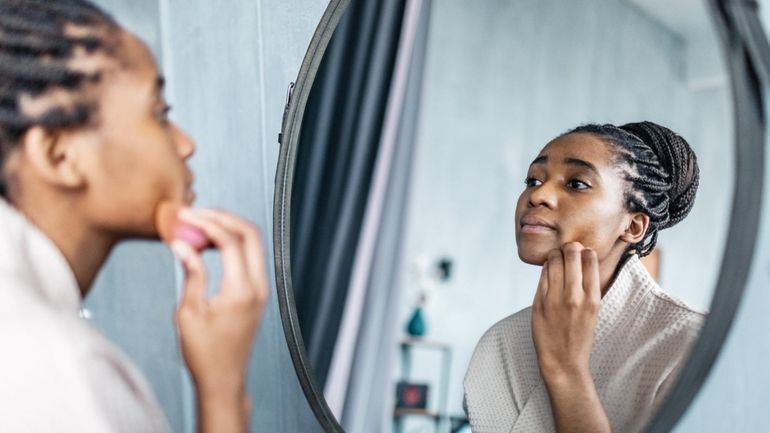 Young adult black woman in bathrobe applying concealer in the...