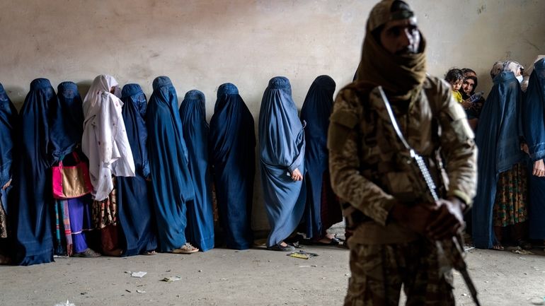 A Taliban fighter stands guard as women wait to receive...