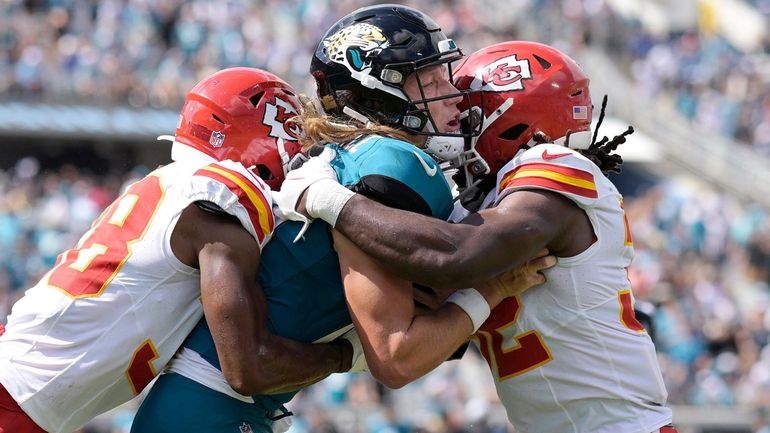 Jacksonville Jaguars quarterback Trevor Lawrence, center, is hit by Kansas...