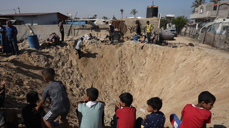 Palestinian children sit at the edge of a crater after...