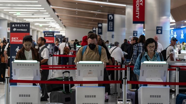 Travelers use kiosks to check in for flights in the...