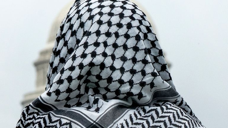 A man wearing a keffiyeh looks at the U.S. Capitol...