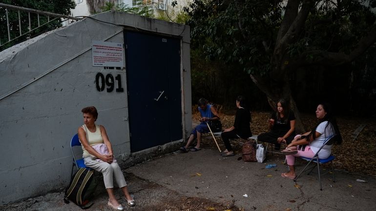 Israelis sit next to a public bomb shelter to stay...