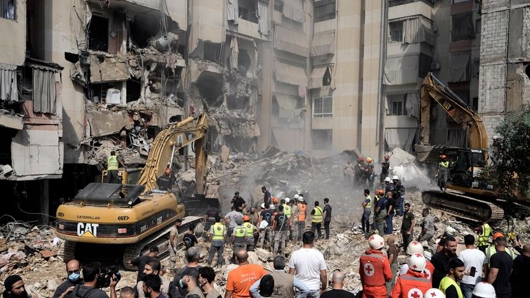 Emergency workers use excavators to clear the rubble at the...