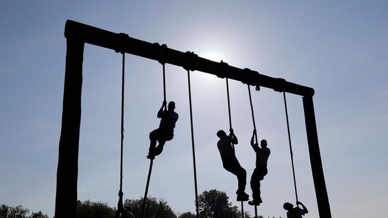 Freshman midshipmen, known as plebes, climb ropes on an obstacle...