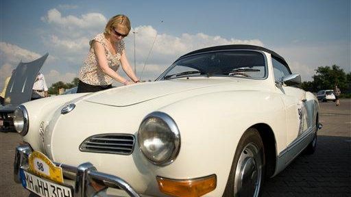A woman inspects a classic Karmann Ghia car.