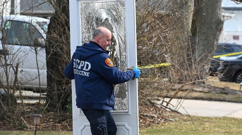 Suffolk County police remove a shattered door as they investigate...