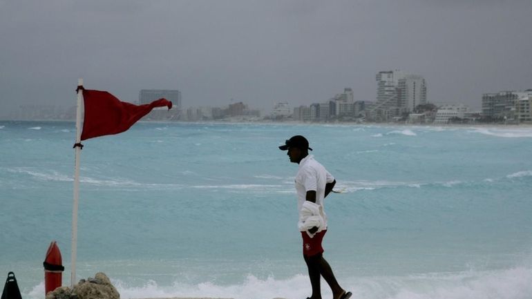 A lifeguard stands next to a red flag meaning high...