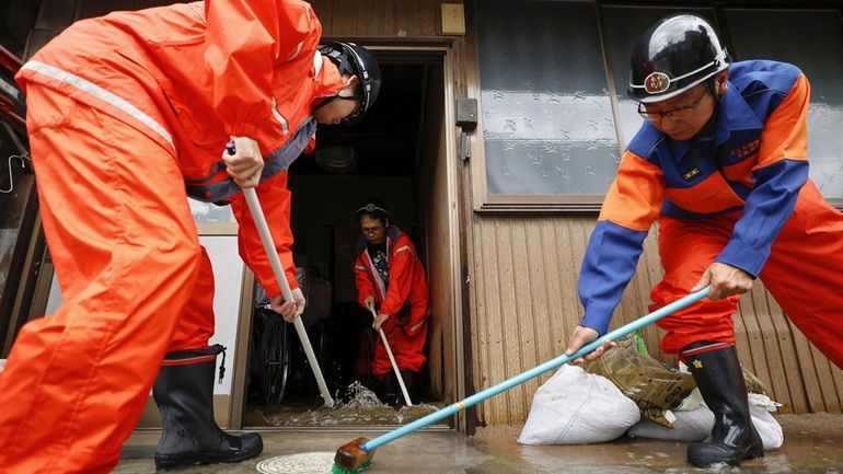 Firefighters help clean up floodwater out of a house in...