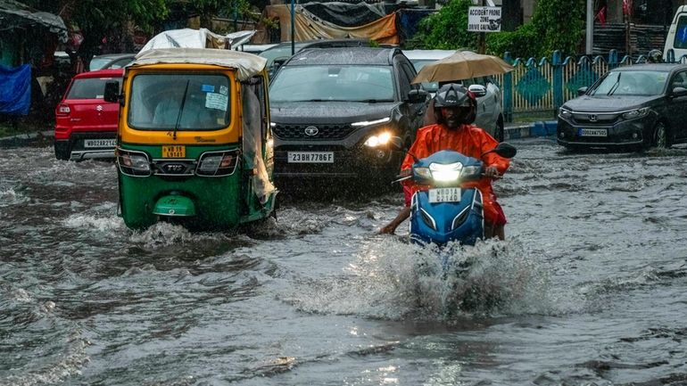 Vehicles move through a waterlogged street in Kolkata, India, as...