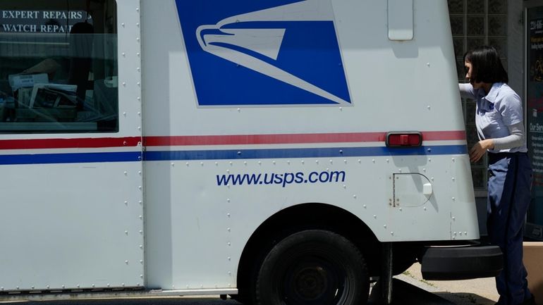 A U.S. Postal Service employee works outside as she makes...