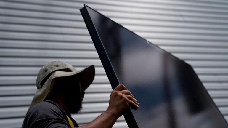 An employee of NY State Solar installs solar panels on a...