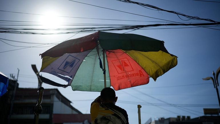 A vendor prepares his umbrella as hot days continue in...