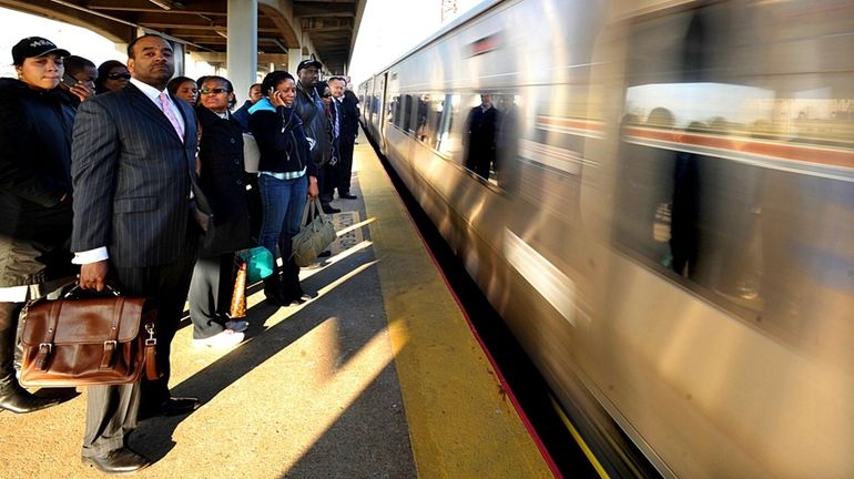 Commuters wait to board an incoming westbound train at the...