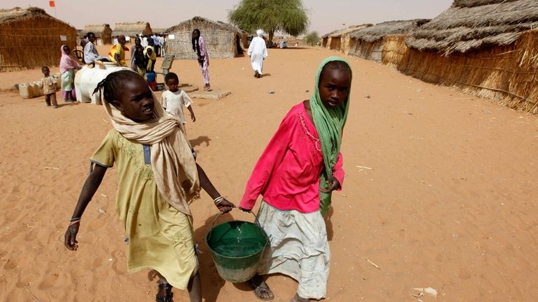 Sudanese refugee girls carry water supplies near a polling station...