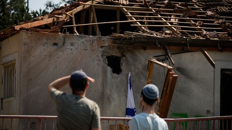 People look at a damaged house that was hit by...