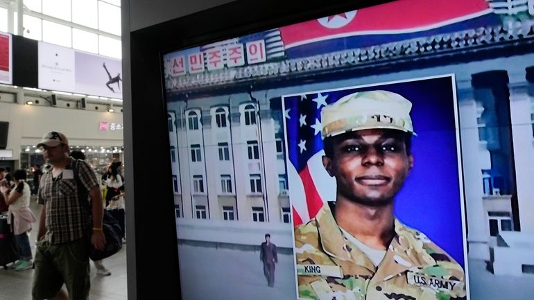 A television screen shows a file image of Pvt. Travis...