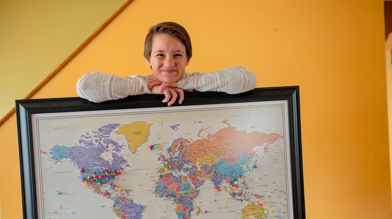 Paula Pecorella holds a world map, on which she's marked all...