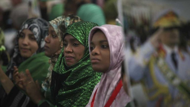 Women sit near a picture of Libyan leader Moammar Gadhafi...