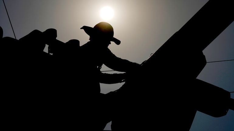 A linesman works on power lines under the morning sun,...