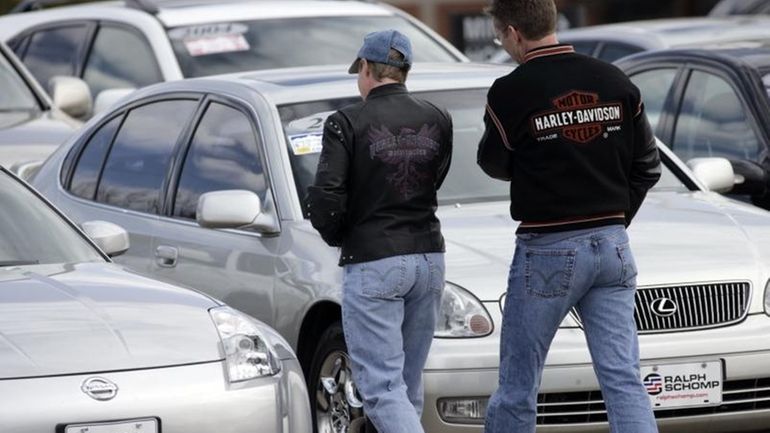 Shoppers look over unsold used vehicles at a dealership in...