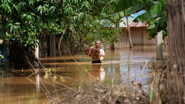 A man carrying a dog wades through a flooded road...