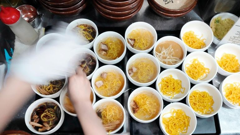 A staff member prepares small bowls of noodle for participants...