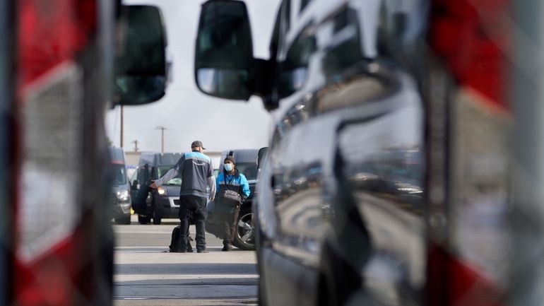 Amazon drivers wait next to their delivery vans after logistics...