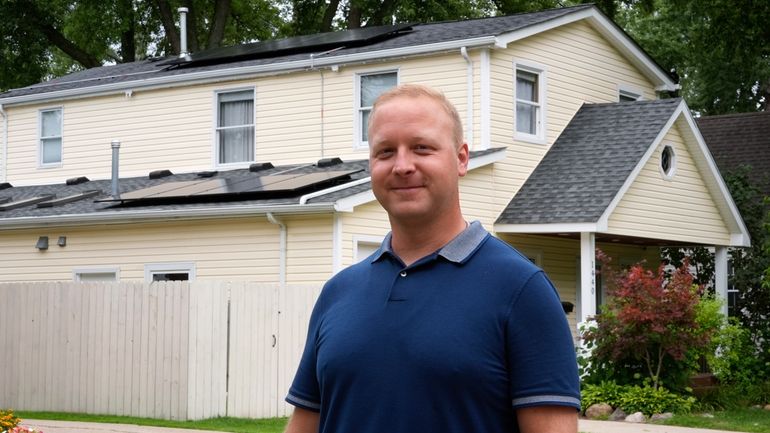 Jason Benedict poses with solar panels on his home in...