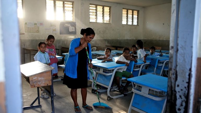 A school teacher sweeps the floor of a classroom before...