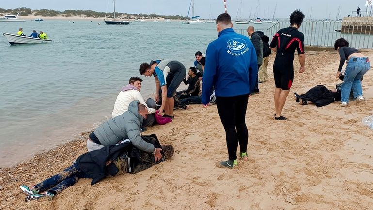 Migrants are rescued by locals on the shore of a...