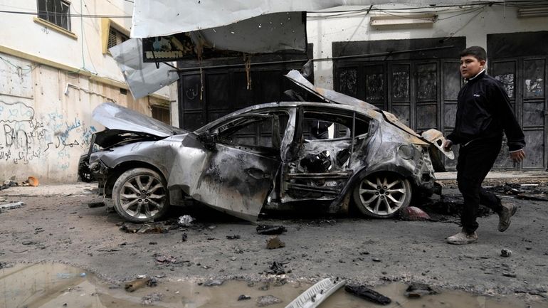 A Palestinian boy walks past a car destroyed in an...