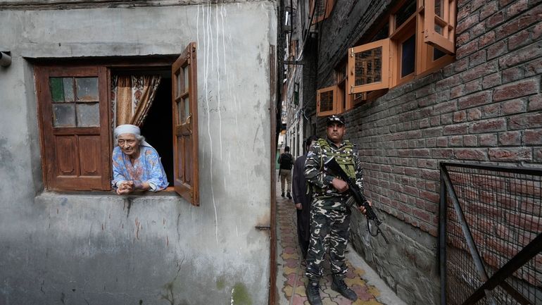 An elderly Kashmiri woman looks on as a paramilitary soldier...