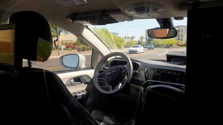 A Waymo minivan moves along a city street as an...