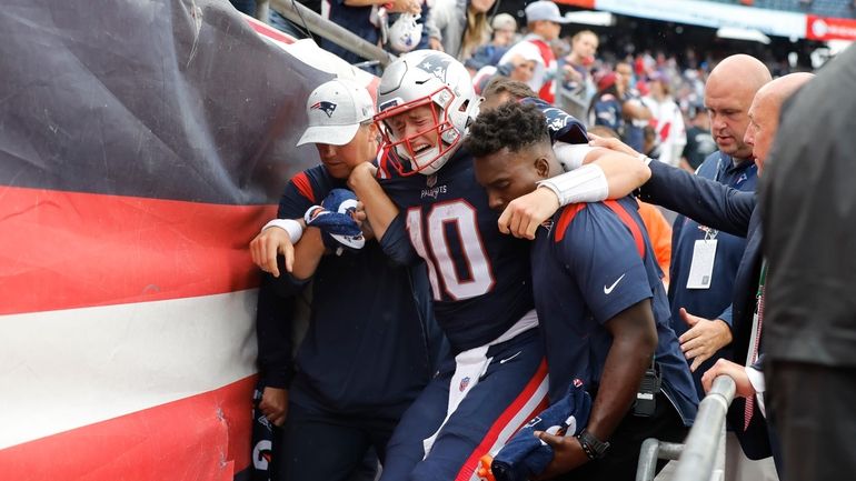 New England Patriots quarterback Mac Jones (10) is helped off...